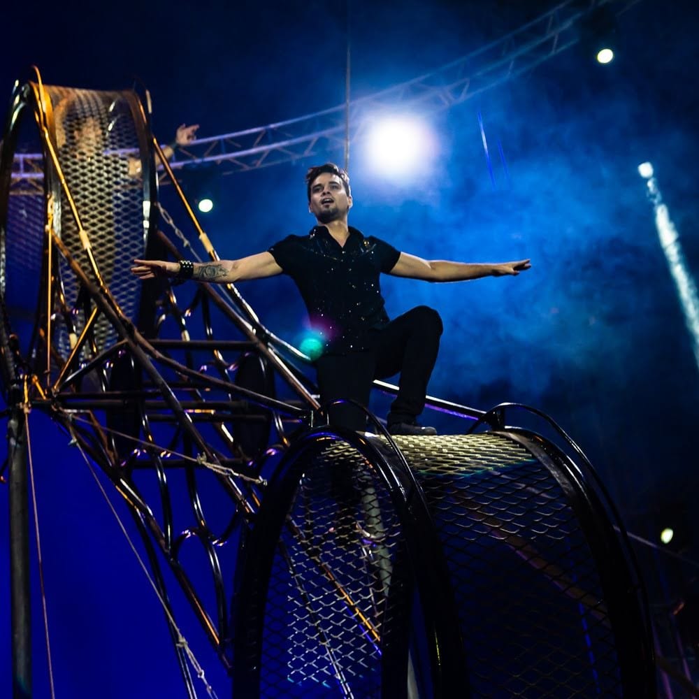 Rodrigo Gomez seated on the wheel with an arm out, Le Cirque Amar.